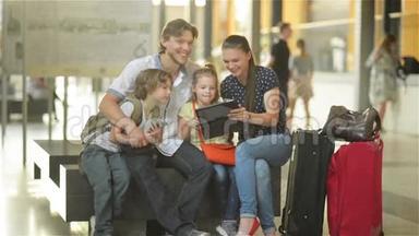 一个大家庭的成员坐在机场或机场的候机室里，在平板电脑上观看度假照片